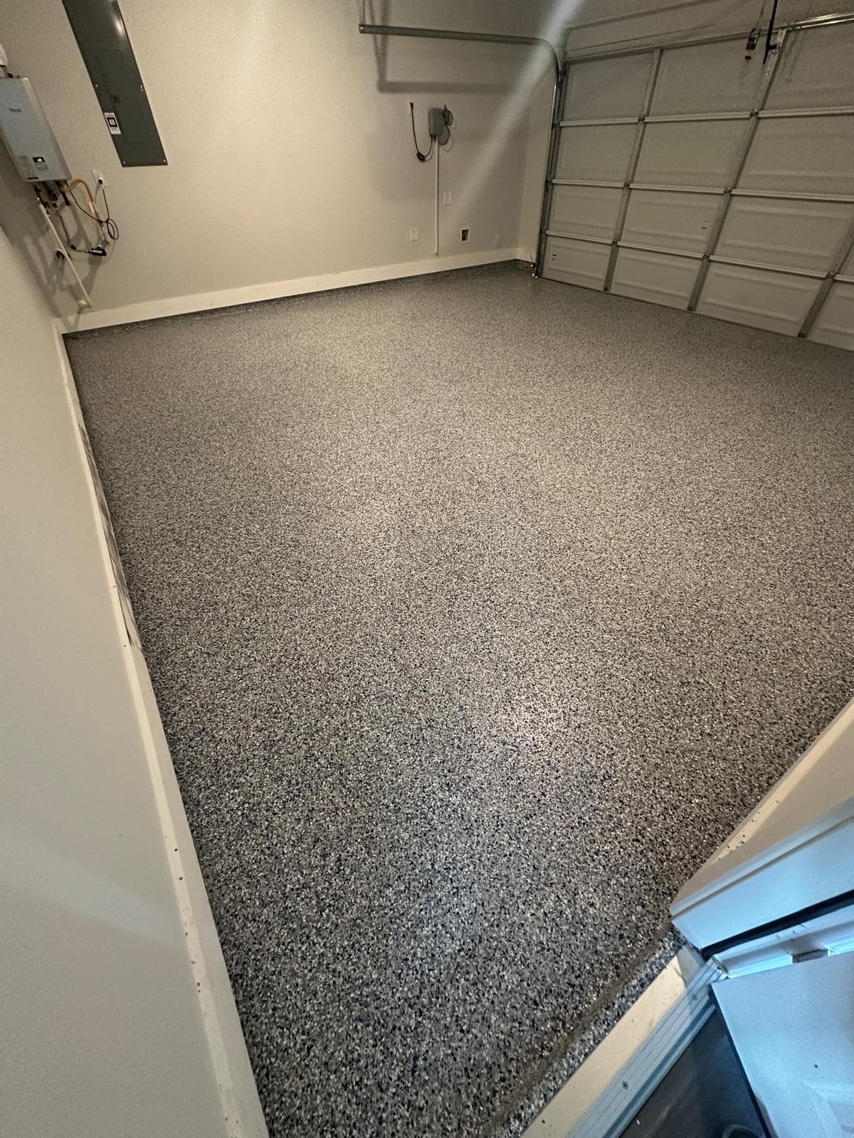 Finished two-car garage floor in an off-white and grey flake blend with navy chips, looking across the bay toward the closed garage door.